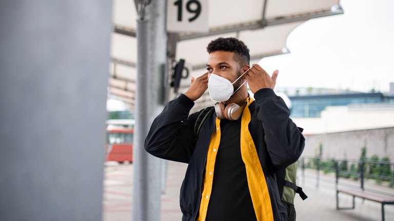 Portrait of male commuter at a bus station putting on face mask.