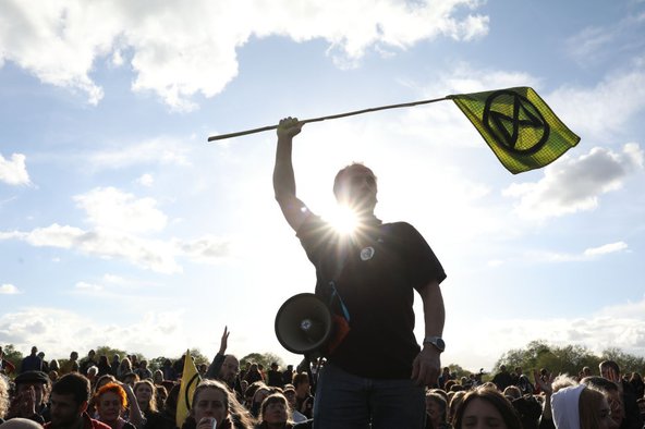 A protester waving the Extinction Rebellion flag, with a crowd of protesters in the background.