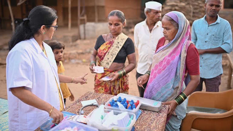 A doctor explaining medicine dosage and giving out medicines to village women during a medical health care camp