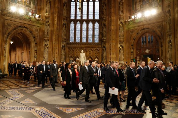 Rows of MPs in suits walk through the ornamental Parliament building.